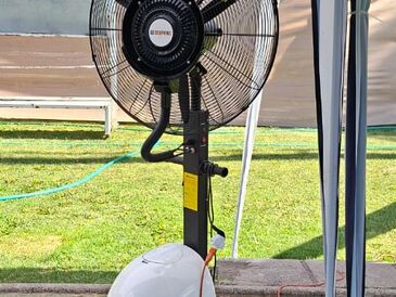 Ventilador con nebulizador en un patio con pasto bajo un toldo